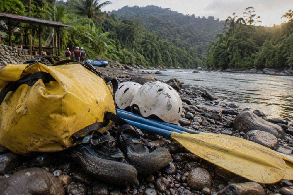 Dry bag and river shoes arranged on a bench beside stacked paddles and helmets