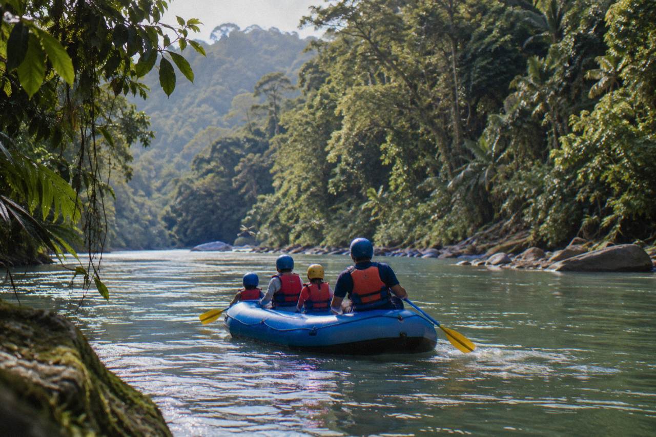 Family raft with paddlers in helmets and life jackets on a calm green jungle river section