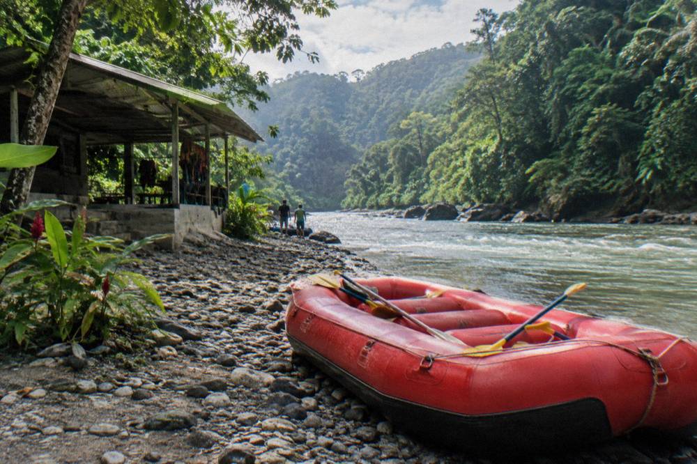 A gravel riverbank in rainforest with an inflated raft waiting at the water's edge
