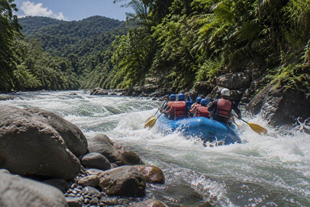 A group of rafters in helmets and life jackets paddling through a foaming rapid.