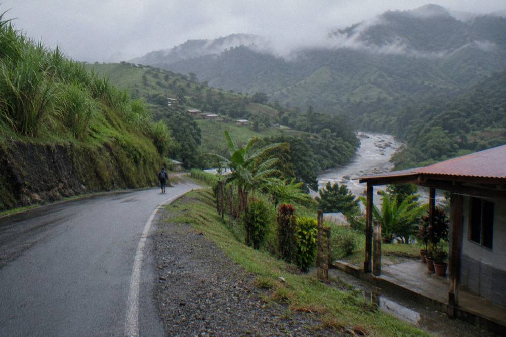 A winding two-lane road through green hills with mist on the ridgelines.