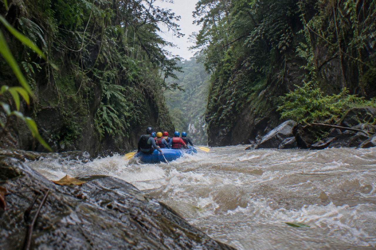 A raft cutting through a narrow jungle gorge with steep green canyon walls rising on both sides.