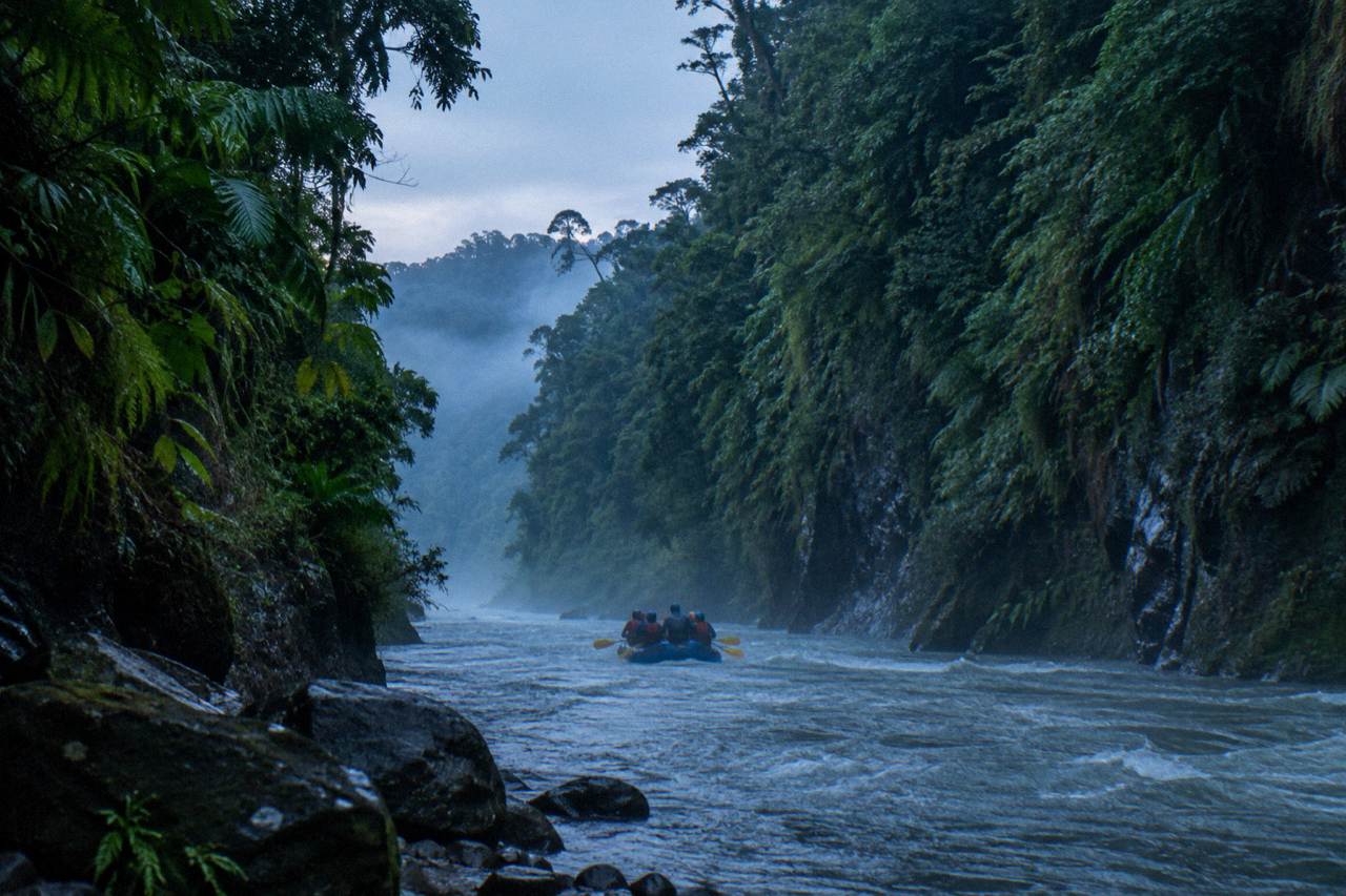 A raft cutting through a narrow jungle gorge with green walls rising on both sides
