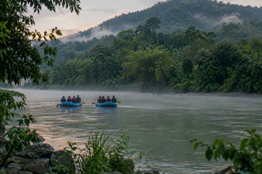 Two rafts floating on wide green water between forested hills in morning light
