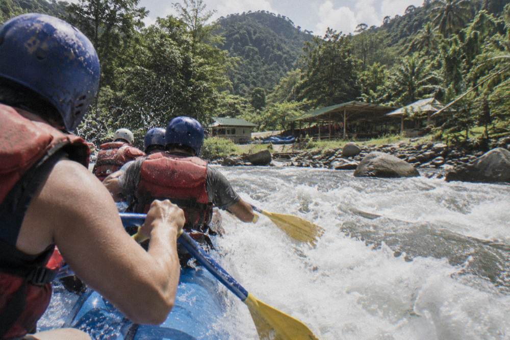 Rafters in helmets and life vests paddling in unison through a foaming rapid