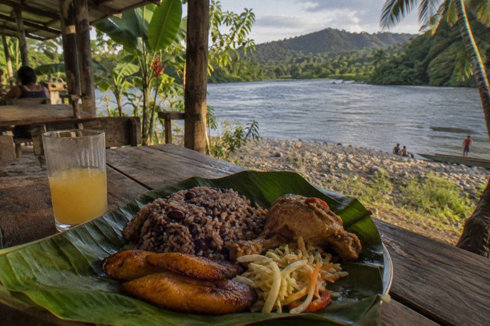 A spread of rice, beans, plantains and chicken served on a banana leaf at a riverside table