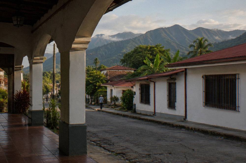 Quiet colonial-era town street with green mountains rising behind the rooftops