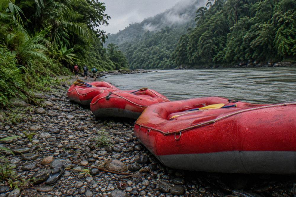 Rafts lined up on a gravel riverbank beside dense green jungle