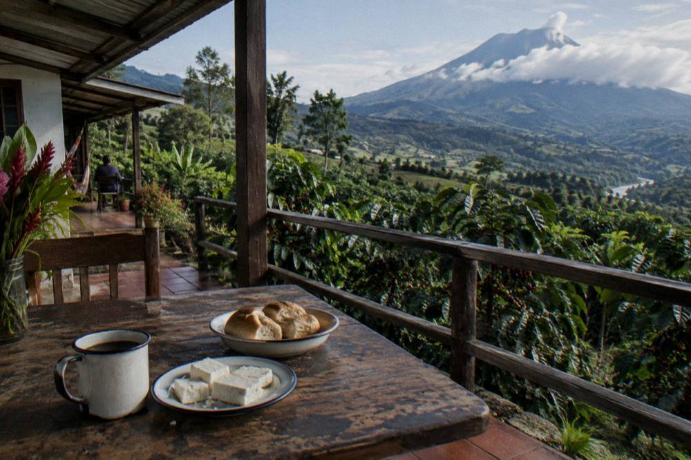 Wooden farm table with fresh coffee, cheese and bread on a hillside veranda