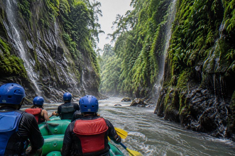 A green raft drifting through a narrow rainforest canyon with waterfalls on the rock walls