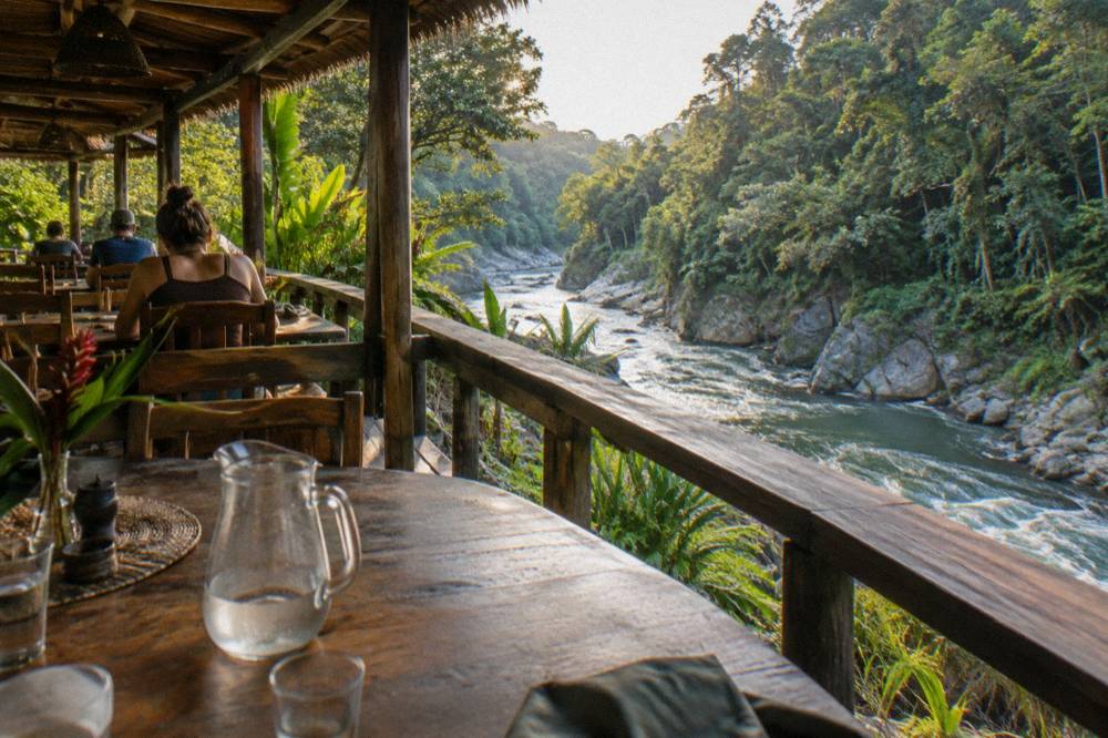 A dining terrace at a wooden jungle lodge overlooking the river gorge in late afternoon light