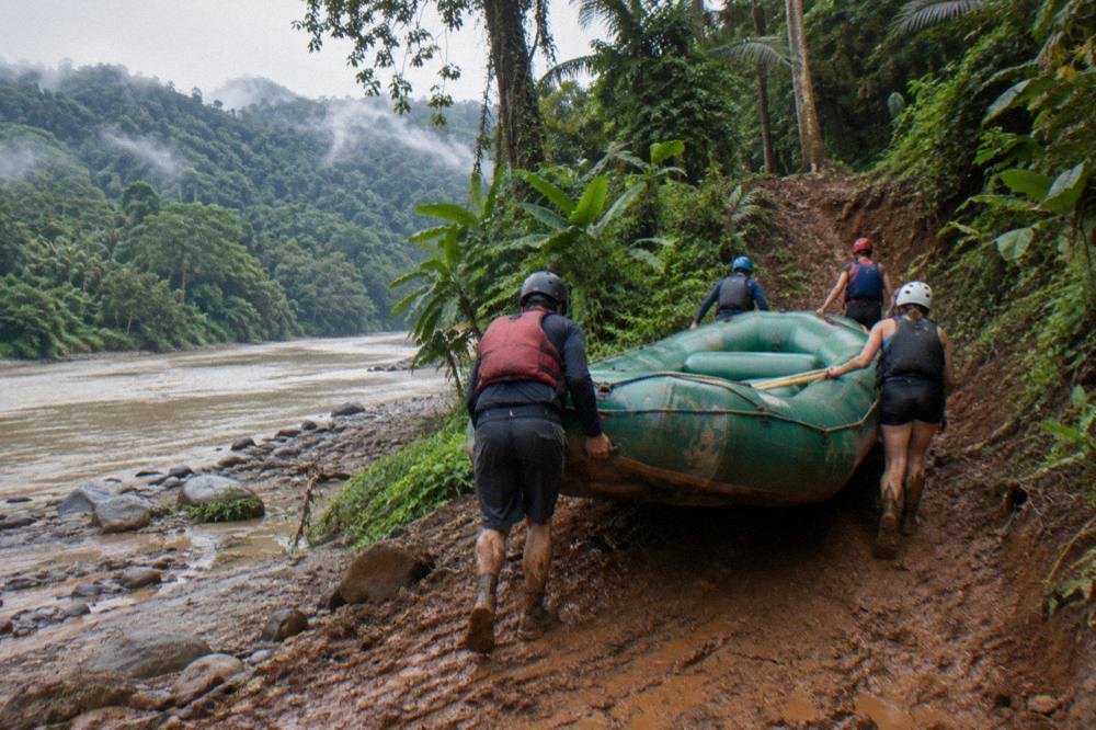 A raft carried up a muddy riverbank toward a trail head in tall rainforest