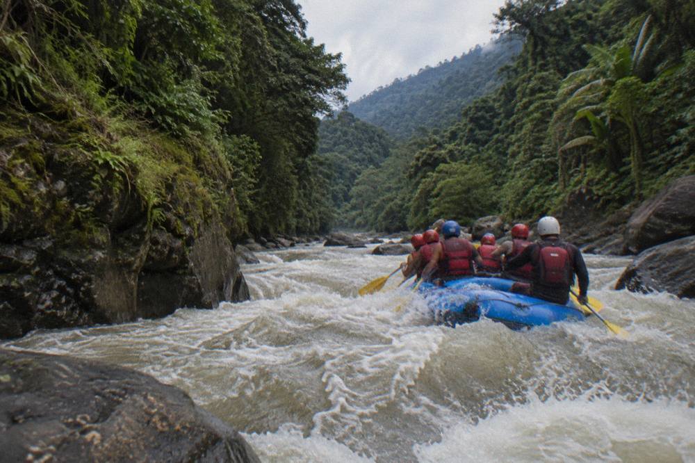 A raft team paddling through a foaming rapid between steep jungle walls