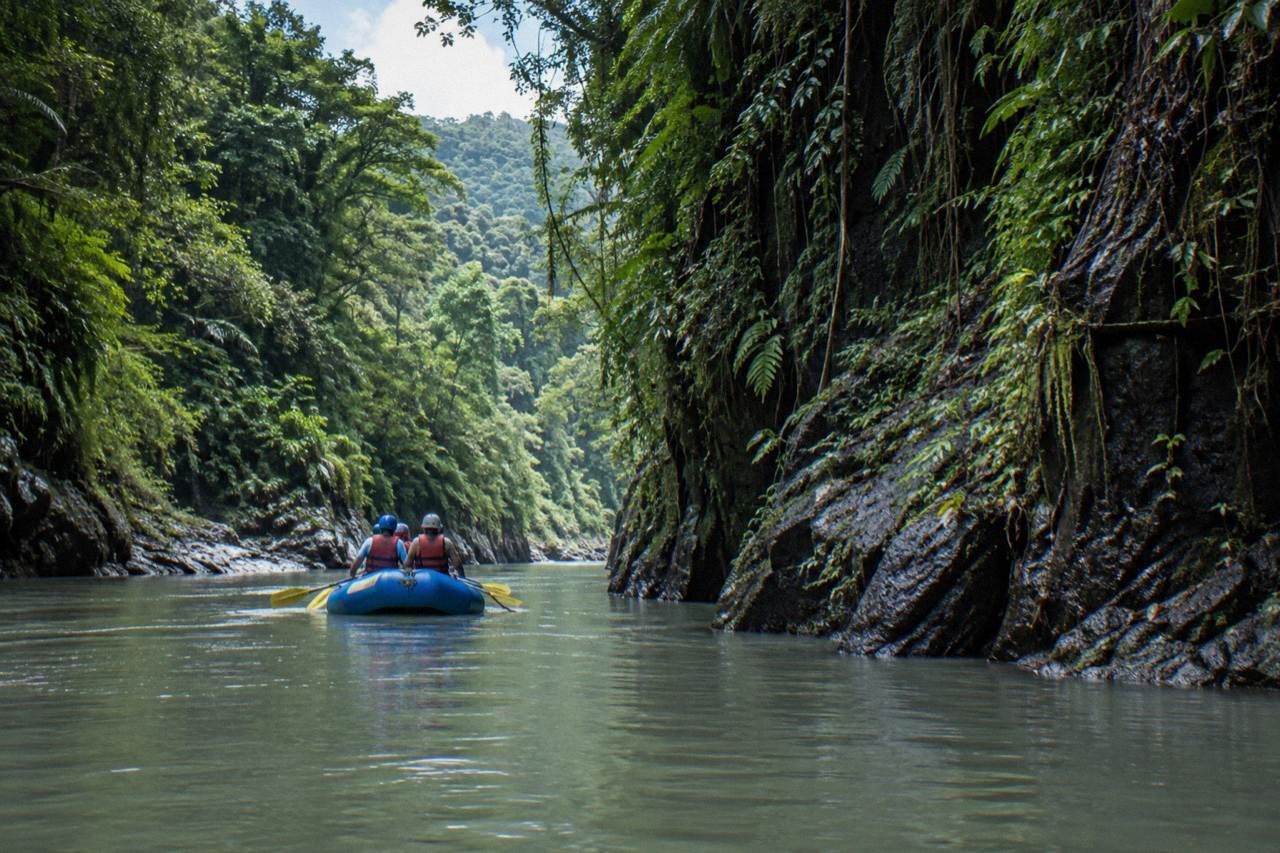 A raft floating through a narrow green rainforest canyon on a tropical river
