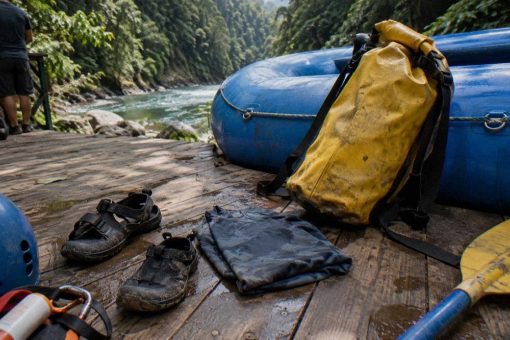Neoprene sandals, quick-dry shirt, sunscreen and a dry bag arranged on a wooden bench