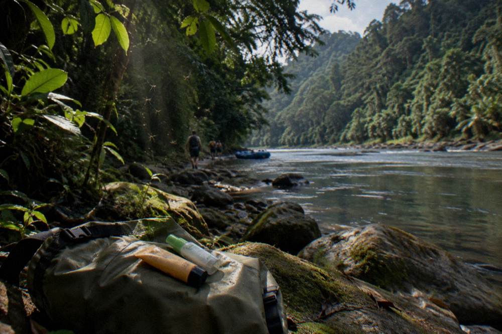 Sunscreen tube and insect repellent bottle resting on a dry bag in jungle shade