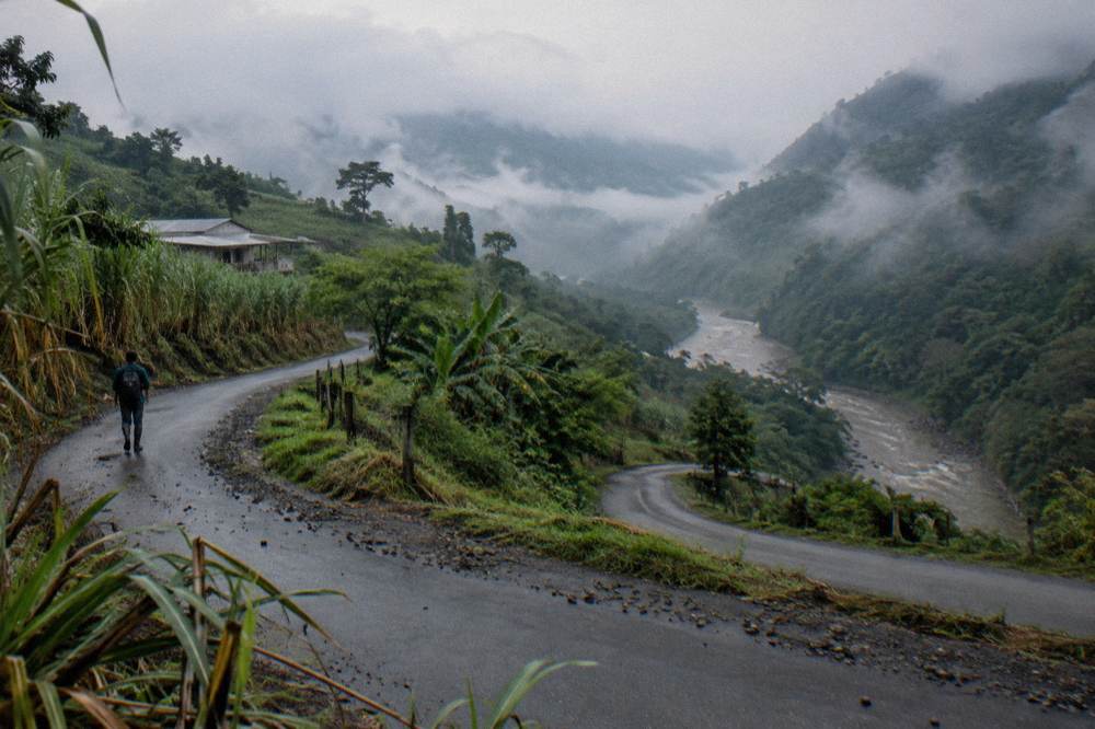Winding two-lane road through green mountains with mist over the valley