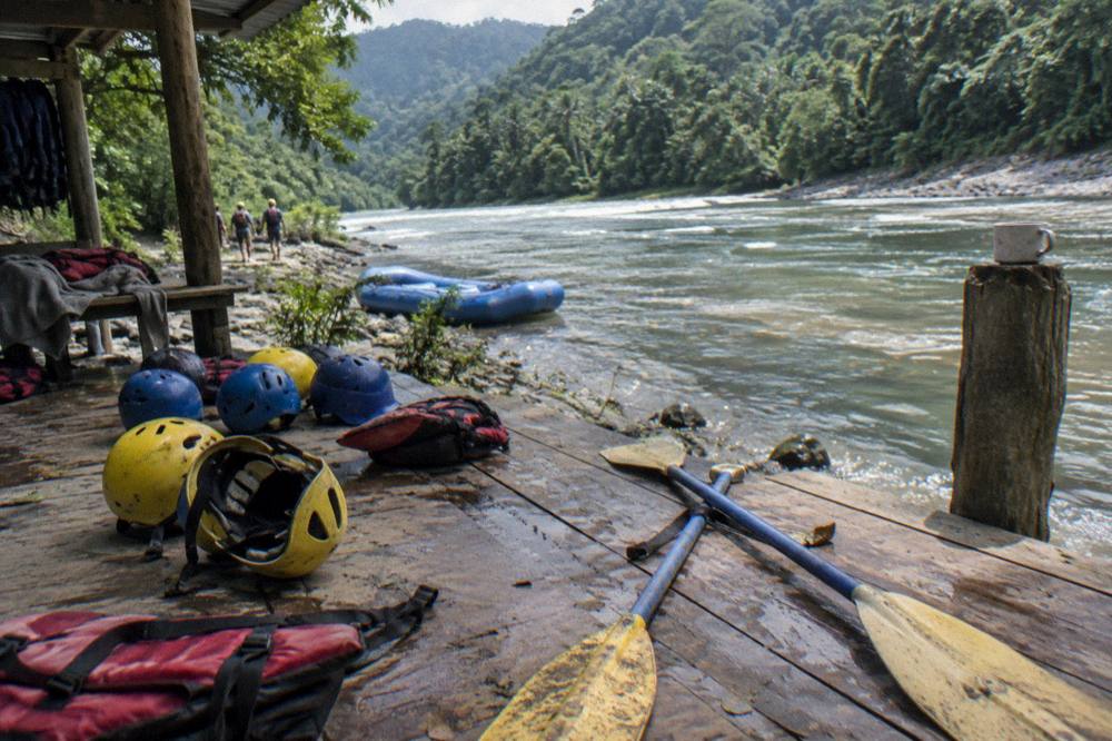 Rafting helmets and paddles laid out on a riverside platform beside calm water