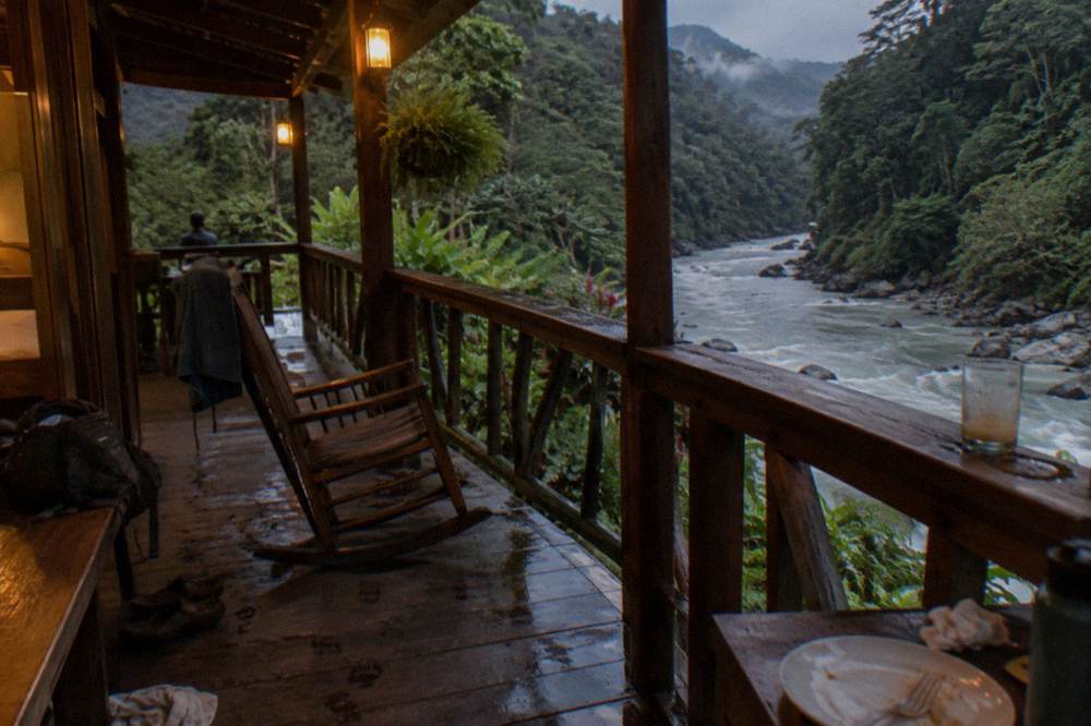 A wooden riverside lodge balcony overlooking the jungle river at dusk