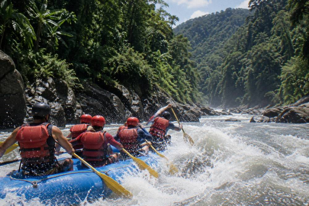 A raft crew paddling in unison through a standing wave in bright daylight