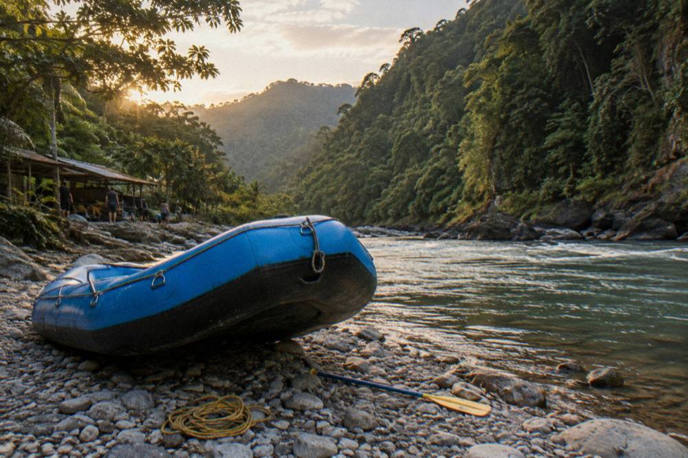 A raft resting on a gravel riverbank with dense rainforest rising on both sides