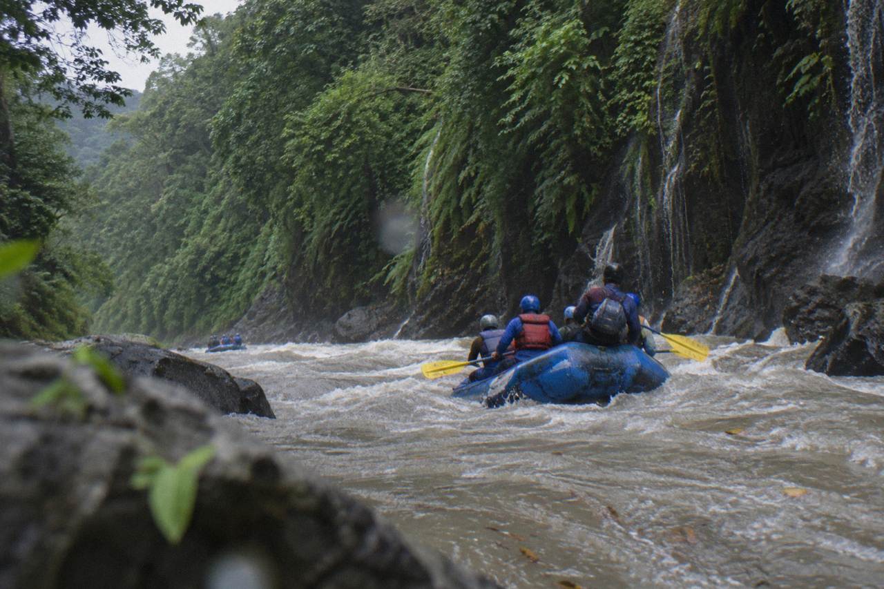 A raft cutting through a green jungle gorge with waterfalls on the canyon walls